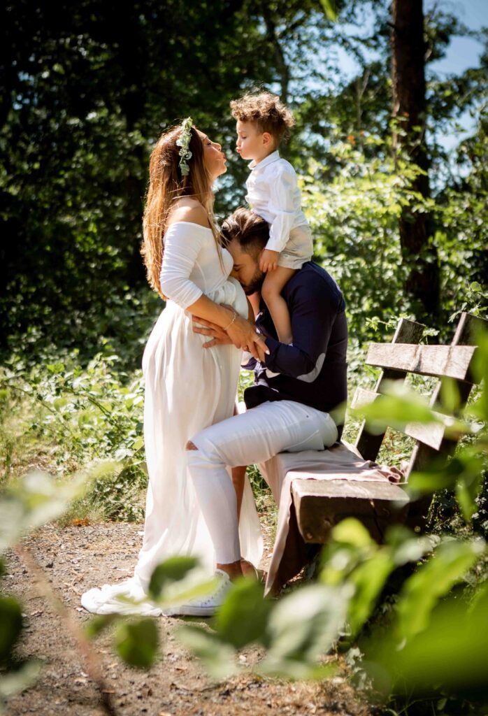 Zärtlicher Familienmoment: Papa mit Sohn auf der Schulter küsst den Babybauch der Mama