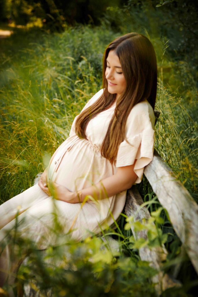 Glückliche werdende Mutter sitzt auf einer Bank und hält ihren Babybauch