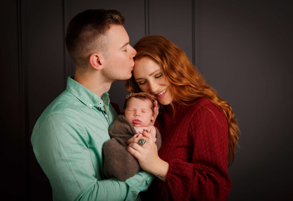 Vater hält das Baby im Arm und küsst die Mutter liebevoll auf die Stirn