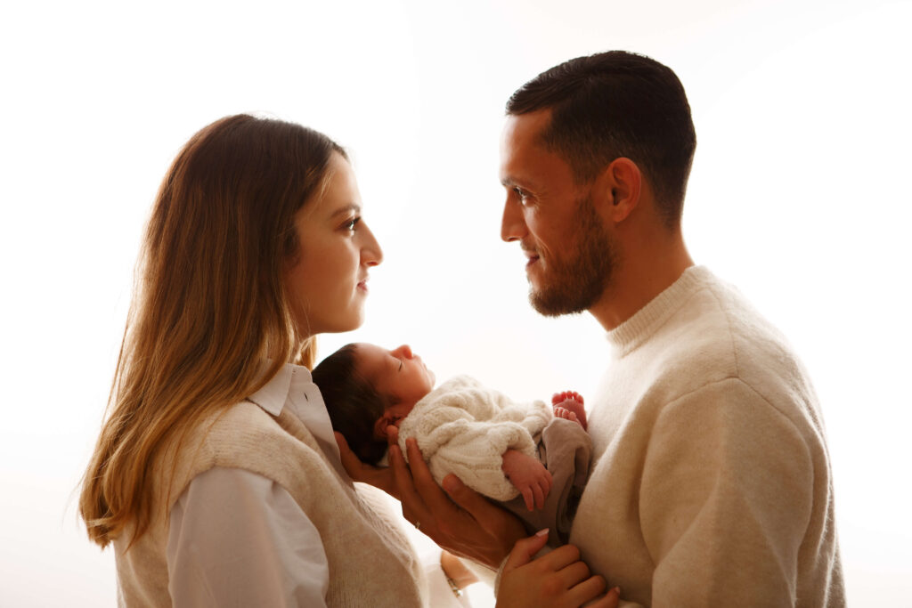 Vater hält liebevoll sein Baby im Arm, während die Mutter glücklich danebensteht.