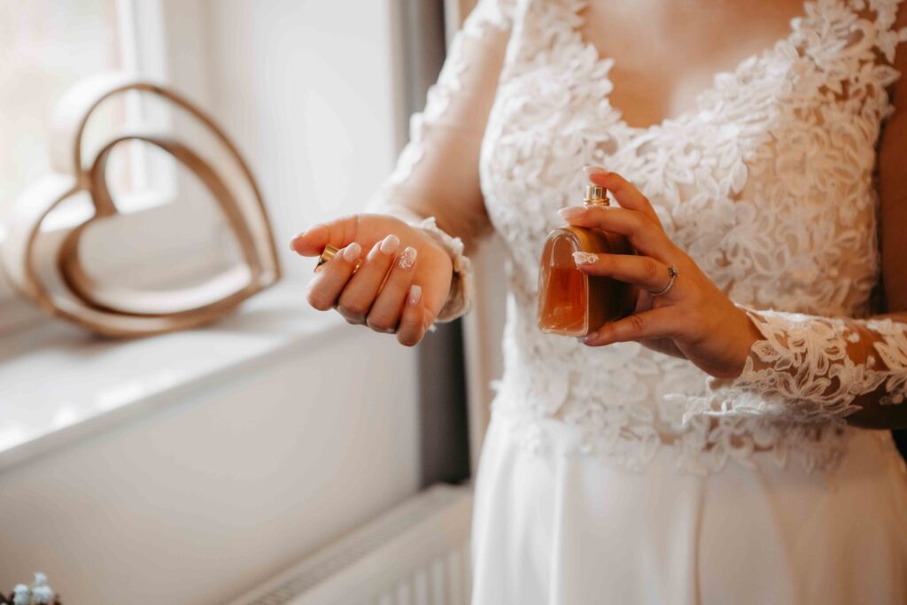 Braut hält Parfumflakon und trägt Duft auf