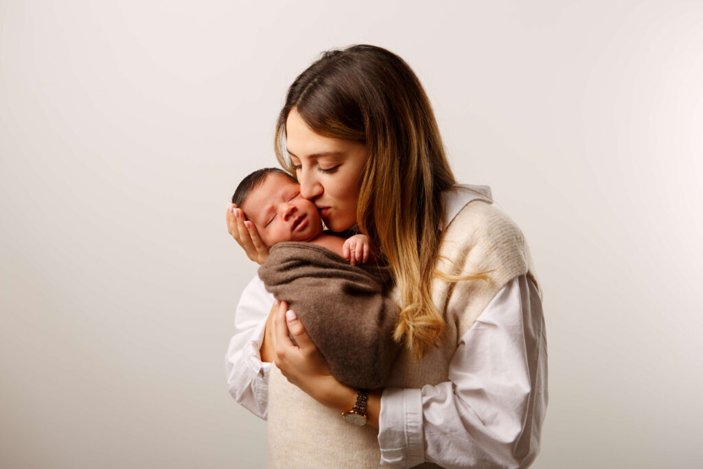Mutter hält ihr Baby liebevoll im Arm und küsst es sanft.
