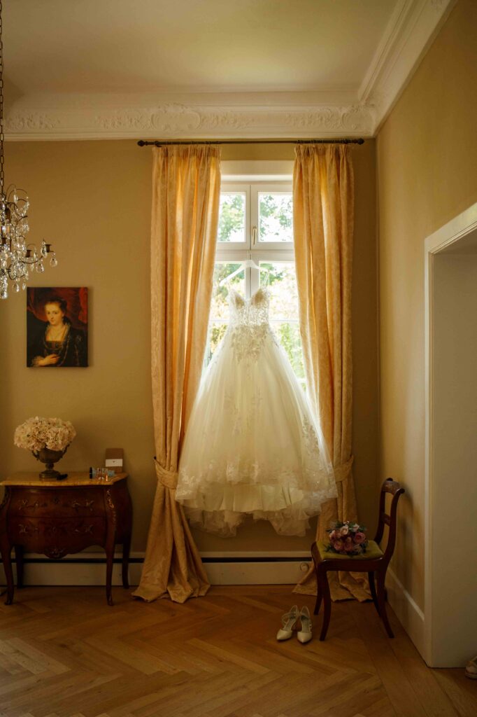 Hochzeitskleid hängt am Fenster und wird vom Tageslicht beleuchtet