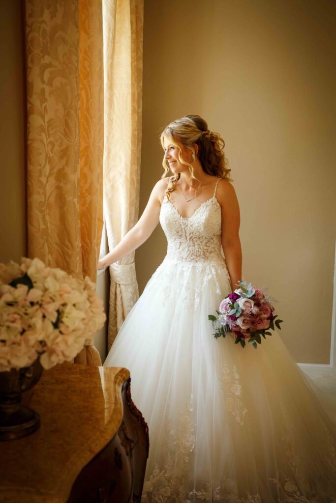 Nachdenkliche Braut schaut im Hochzeitskleid aus dem Fenster