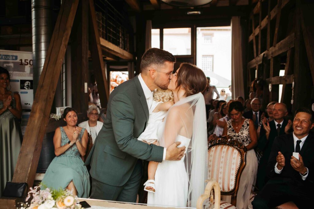 Brautpaar beim Kuss im Standesamt, Gäste applaudieren