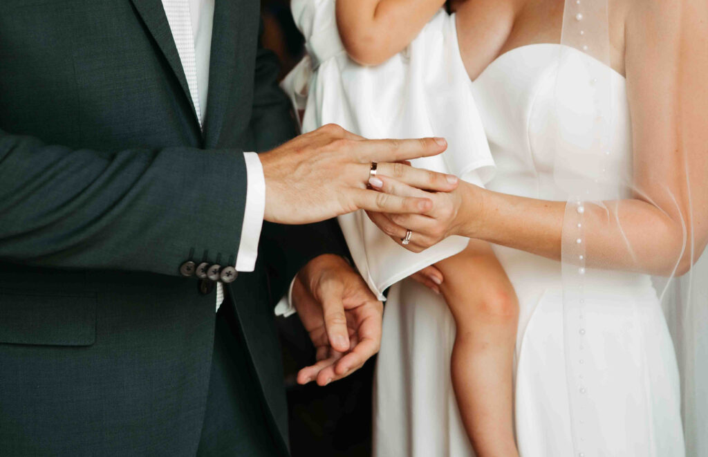 Braut steckt Bräutigam den Ring an – Detailfoto der Hände