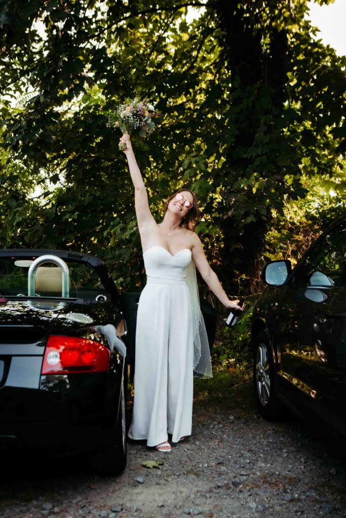 Strahlende Braut posiert neben dem Auto