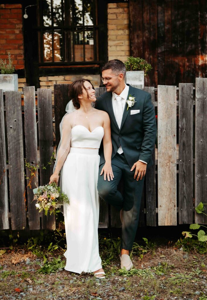 Hochzeitsfoto: Brautpaar posiert am rustikalen Holzzaun