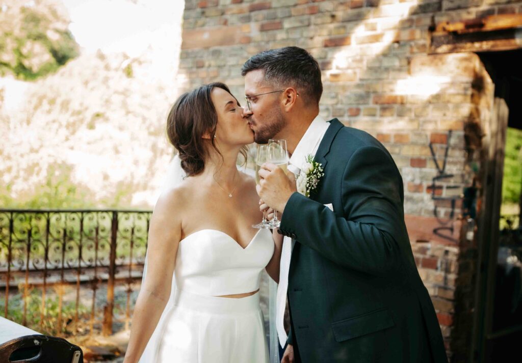 Brautpaar küsst sich und hält Sektgläser in der Hand