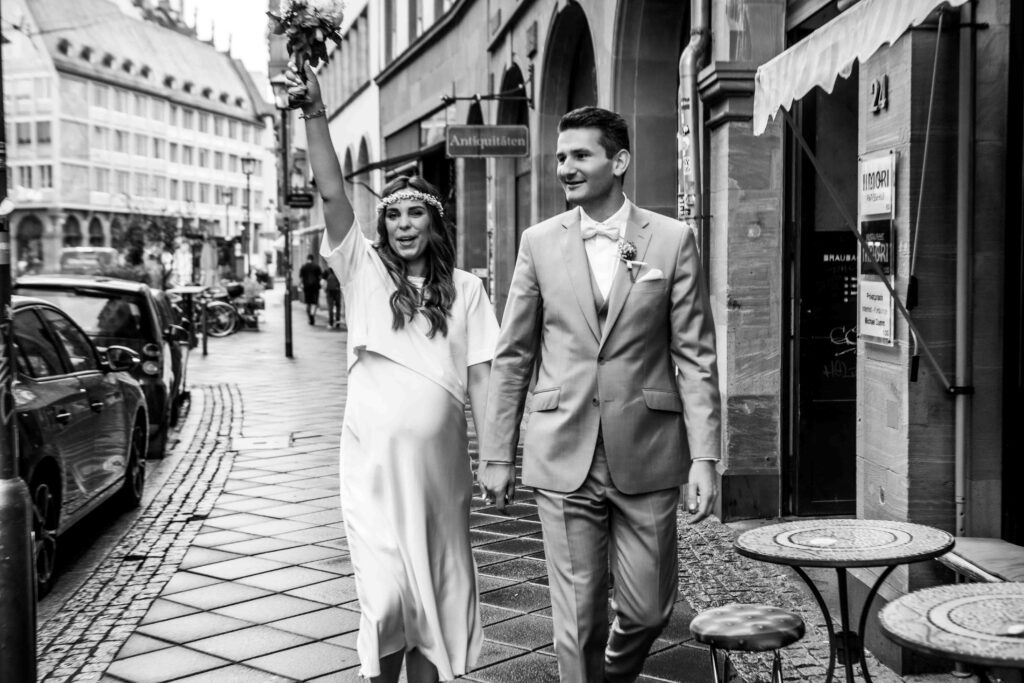 Braut und Bräutigam gehen Hand in Hand, Braut hebt den Strauß in die Luft