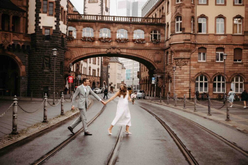 Braut und Bräutigam überqueren die Straße, Hand in Hand und leicht versetzt
