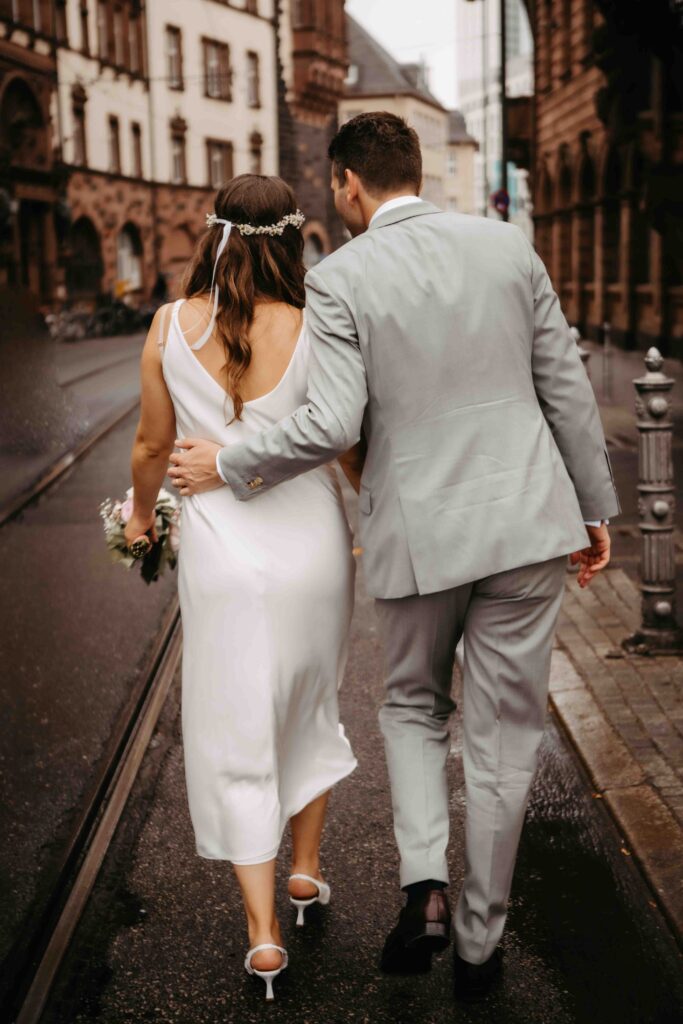 Brautpaar spaziert durch Frankfurt, Bräutigam hält Braut an der Hüfte