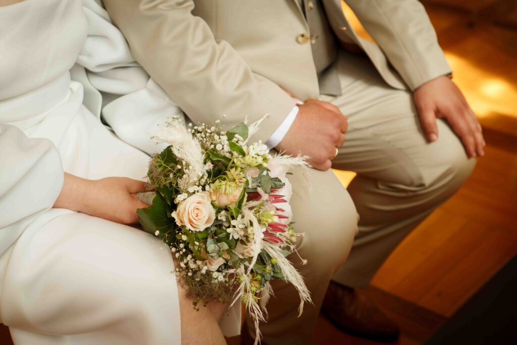 Detailaufnahme: Brautpaar hält sich an den Händen, Brautstrauß sichtbar