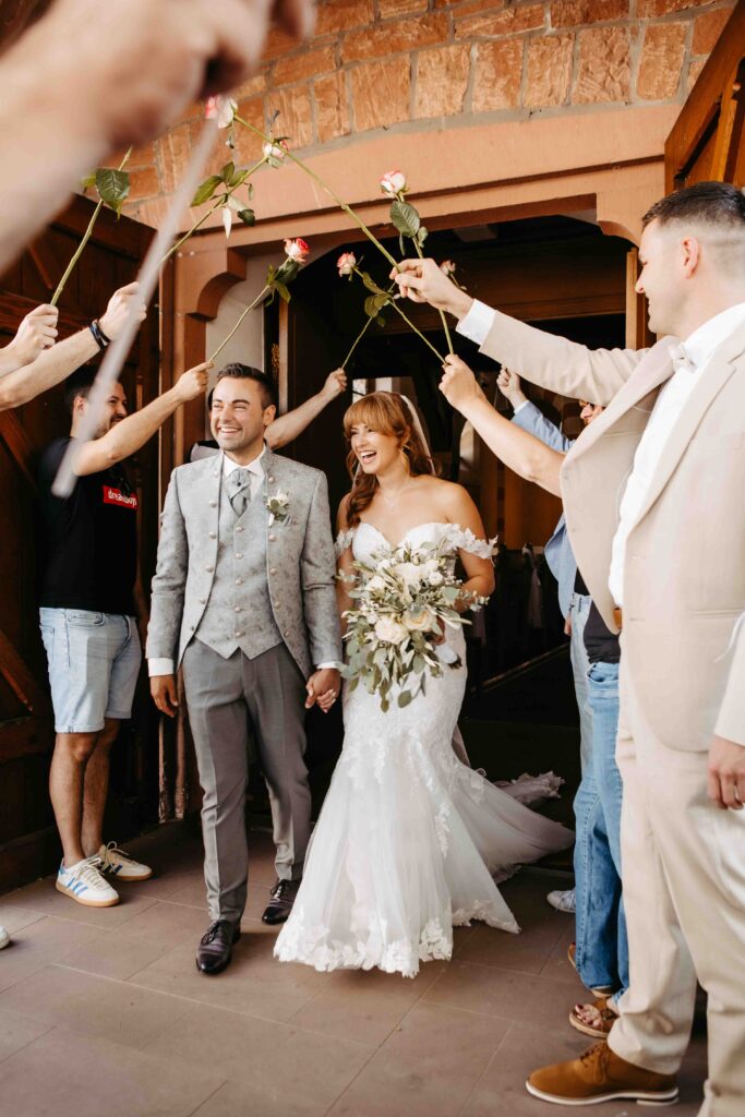 Brautpaar kommt aus der Kirche gäste halten Rosen hoch.