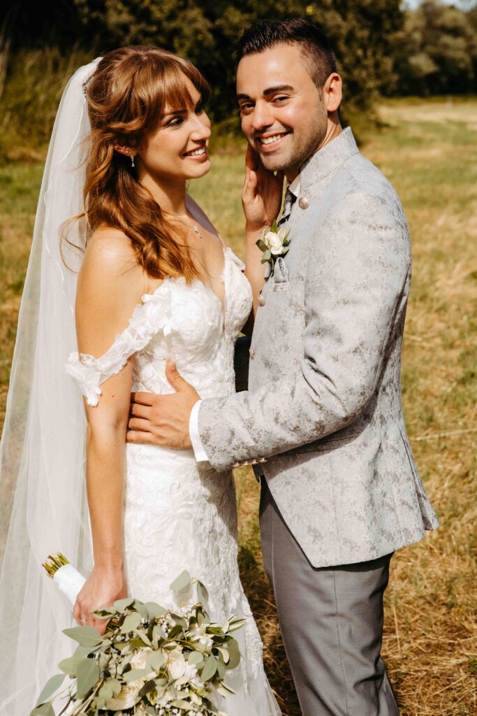 Die die Braut schaut ihren Mann vierliebt an, er schaut in die Kamera.